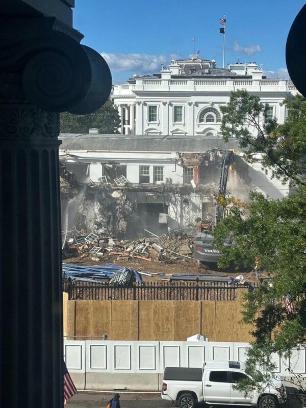 Demolition vehicle tearing down wall of White House wing.